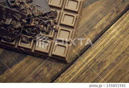Flat vector milk chocolate bar is resting on weathered plank, revealing dark shards and shavings Flat vector milk chocolate bar is resting on weathered plank, revealing dark shards and shavings 133851591