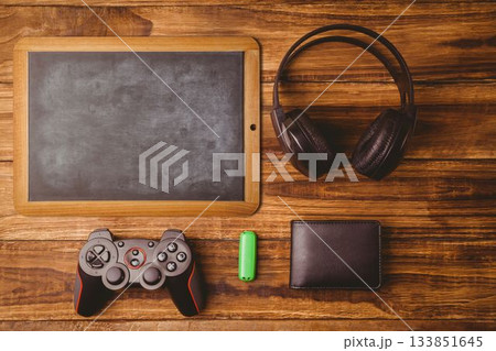 Showing flat top-down scene with wooden chalkboard, headphones, controller, green USB drive, wallet Showing flat top-down scene with wooden chalkboard, headphones, controller, green USB drive, wallet 133851645