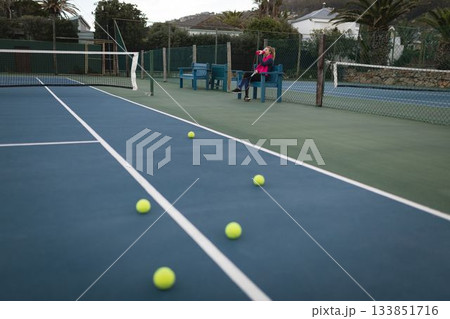 Child holding water bottle is sitting on blue bench by tennis court in flat design 133851716