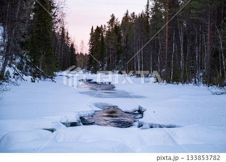 winter river flowing through snowy forest landscape in lapland 133853782