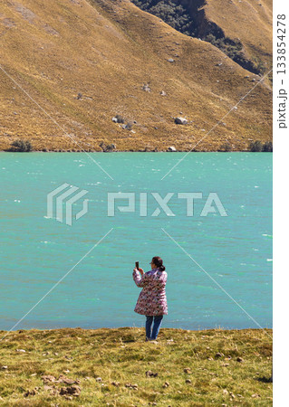 A woman is taking a picture of a lake Querococha, Ancash with a smartphone A woman is taking a picture of a lake Querococha, Ancash with a smartphone 133854278