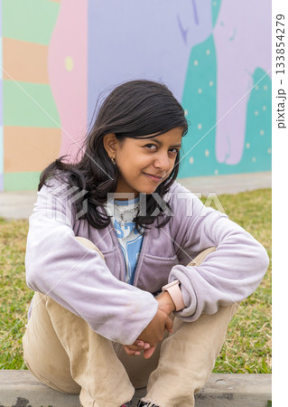 A young girl is sitting on the grass with her hands on her knees A young girl is sitting on the grass with her hands on her knees 133854279