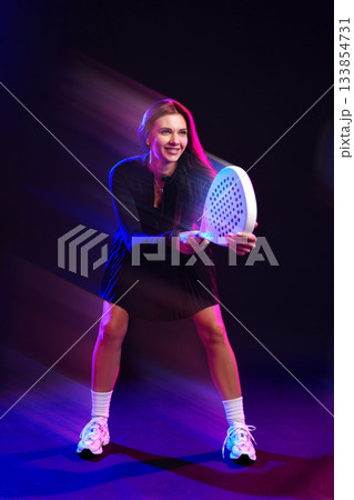 Young woman playing padel with a vibrant background in a dynamic sports setting Young woman playing padel with a vibrant background in a dynamic sports setting 133854731