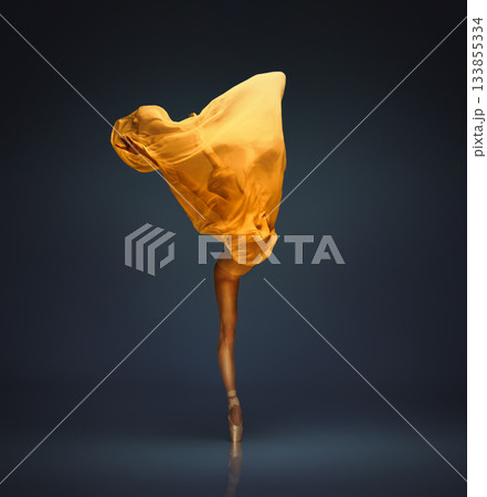 Ballet dancer lifting wide golden fabric shape on dark blue stage light Ballet dancer lifting wide golden fabric shape on dark blue stage light 133855334