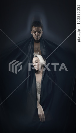 Stylized portrait of two dancers wrapped in dark fabric on deep shadow background. 133855353