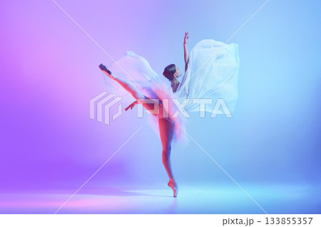 Ballet dancer in expansive high kick with flowing fabric on neon blue-violet stage 133855357