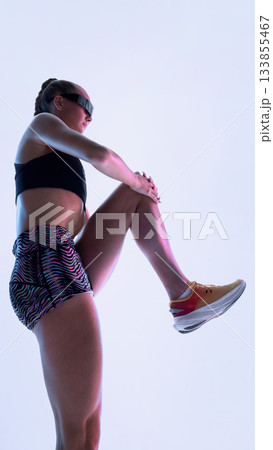 Futuristic female athlete stretching knee upward in neon studio Futuristic female athlete stretching knee upward in neon studio 133855467