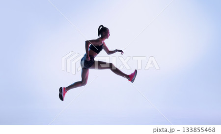 Futuristic female athlete performing dynamic leap in neon light Futuristic female athlete performing dynamic leap in neon light 133855468