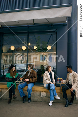Group spending time together with hot drinks outside city cafe in winter weather Group spending time together with hot drinks outside city cafe in winter weather 133855592