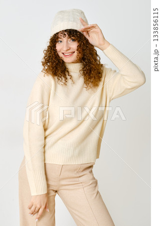 Woman poses smiling in a cozy sweater and hat against a light background in a casual setting 133856115