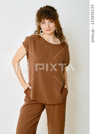 Stylish woman poses in a brown outfit against a plain background in a relaxed setting 133856135