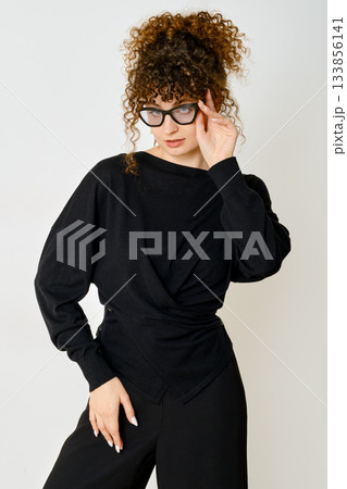 Stylish woman wearing black outfit poses with confidence against simple background 133856141