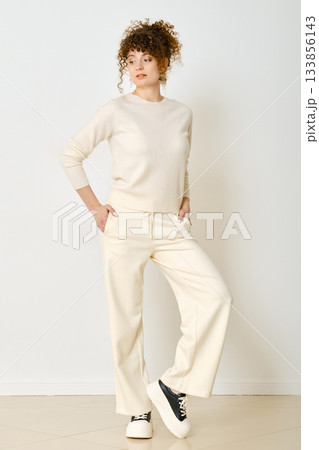 Stylish woman posing in light outfit against white background in a minimalist setting Stylish woman posing in light outfit against white background in a minimalist setting 133856143