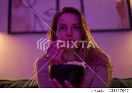 Female watching screen with popcorn bowl on sofa indoors 133857647