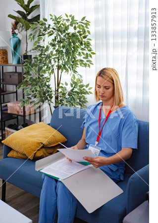 Female Doctor Reading Medical Records Sitting On Sofa At Home Female Doctor Reading Medical Records Sitting On Sofa At Home 133857913