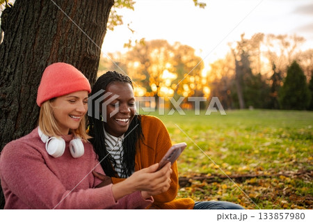 Diverse friends enjoying autumn park looking at smartphone 133857980