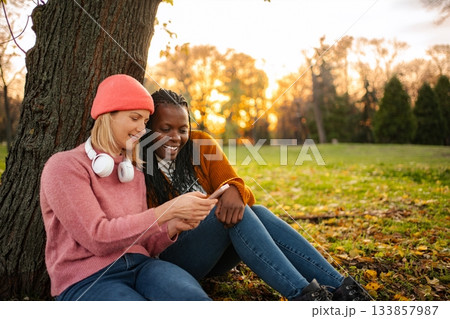 Diverse friends sharing mobile phone content in autumn park 133857987