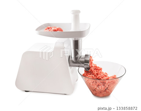 A white electric meat grinder with raw meat pieces on the tray, actively mincing meat into a clear glass bowl, isolated on white. High quality photo A white electric meat grinder with raw meat pieces on the tray, actively mincing meat into a clear glass bowl, isolated on white. High quality photo 133858872