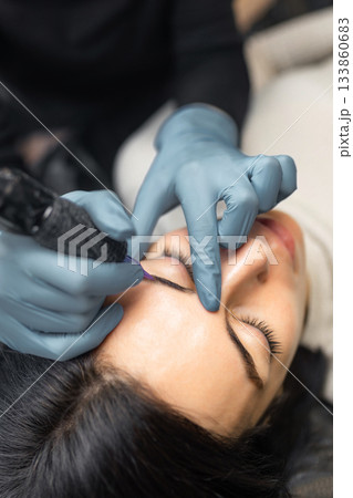 Close up of a cosmetologist performing eyebrow microblading on a female client. Professional beauty procedure, sterile tools, precision work and eyebrow shaping in a modern beauty studio. Close up of a cosmetologist performing eyebrow microblading on a female client. Professional beauty procedure, sterile tools, precision work and eyebrow shaping in a modern beauty studio. 133860683
