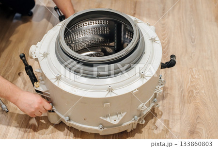 Mechanic repairing a washing machine drum, showing hands-on appliance maintenance at work. 133860803