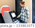 A young man in a plaid shirt uses a self-service machine, focused on inserting a card into the terminal at an indoor location. High quality photo 133861073