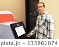 A young man in a plaid shirt uses a self-service terminal, inserting a card, possibly at an airport or station. High quality photo 133861074