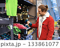 Young man in a red jacket choosing a blue dumbbell in a sports equipment store. High quality photo 133861077