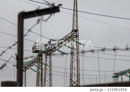 Tall power lines stand against a gray sky near an electric substation, highlighting the infrastructure of energy distribution and security Tall power lines stand against a gray sky near an electric substation, highlighting the infrastructure of energy distribution and security 133861958