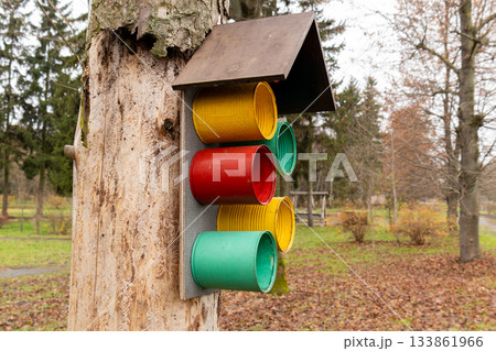 Recycling bins in bright colors are attached to a tree in a public park, encouraging visitors to sort their waste for better environmental care 133861966
