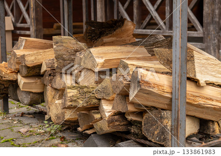 Chopped firewood lies stacked next to a wooden shelter, prepared for winter use in a calm outdoor setting with rustic charm 133861983