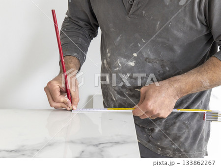 Craftman in grey shirt measures a marble tile using a ruler. Handy men at work, hands closeup 133862267