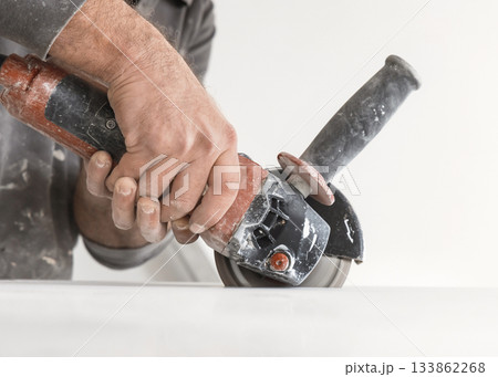 Craftman in grey shirt cuts a gray marble tile using an angle grinder. Handy men at work, hands closeup Craftman in grey shirt cuts a gray marble tile using an angle grinder. Handy men at work, hands closeup 133862268