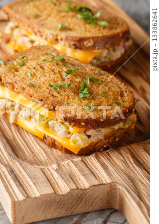 Tuna melt is a sandwich made of bread, tuna and cheese with added vegetables and mayonnaise, close-up on a wooden board. Vertical 133862641