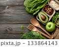 Healthy vegan food ingredients are displayed with utensils on a wooden surface. 133864143