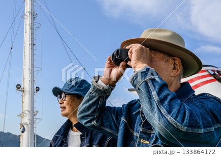 双眼鏡で遠くを見つめるシニア夫婦と船の景色 133864172