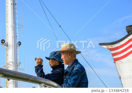 双眼鏡で景色を眺めるデニム姿のシニア夫婦、船上の旅 133864258