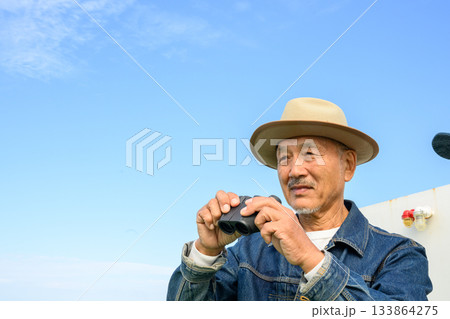 双眼鏡を手に船上から青空と景色を眺める中高年男性 133864275