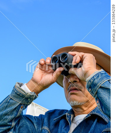 青空を背景に双眼鏡で遠くを見つめるシニア男 133864289