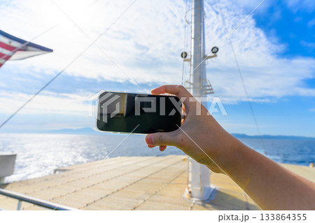 フェリーの甲板でスマートフォンを使い海と空 133864355