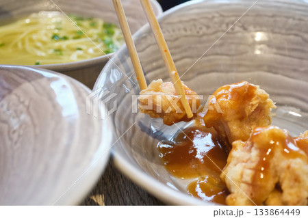 Chopsticks picking up crispy fried chicken coated in sweet sauce from bowl 133864449