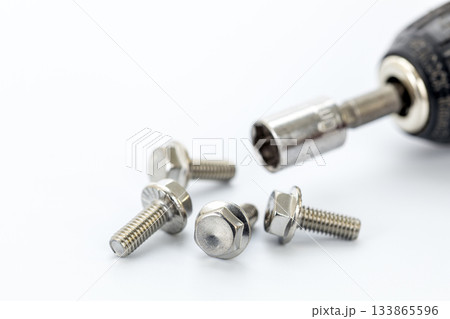 Four steel hex bolts placed on a white surface with a close-up of a socket wrench and metallic socket attachment for hardware 133865596