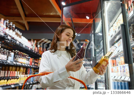 A woman holds a beer bottle in front of a fridge of beers A woman holds a beer bottle in front of a fridge of beers 133866646