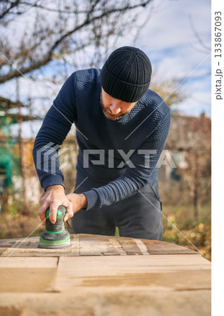Man sanding wooden garden table with sander Man sanding wooden garden table with sander 133867093