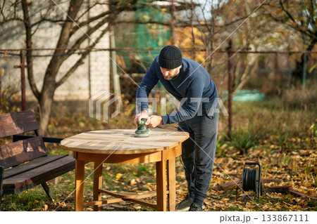 Man sanding wooden garden table with sander 133867111