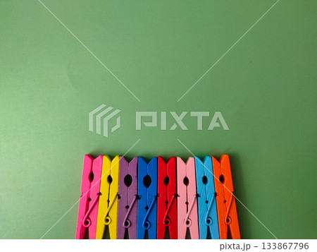 The image shows a row of colorful wooden clothespins on a green background. 133867796