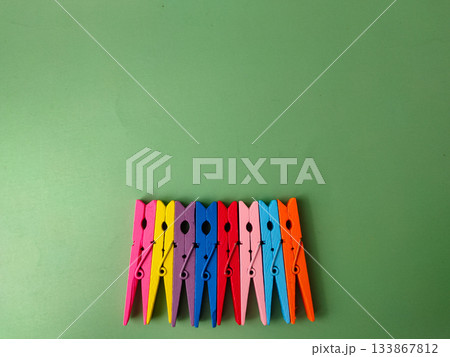 The image shows a row of colorful wooden clothespins on a green background. The image shows a row of colorful wooden clothespins on a green background. 133867812