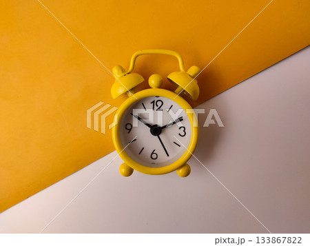 The small yellow analog alarm clock on a white and yellow background. 133867822