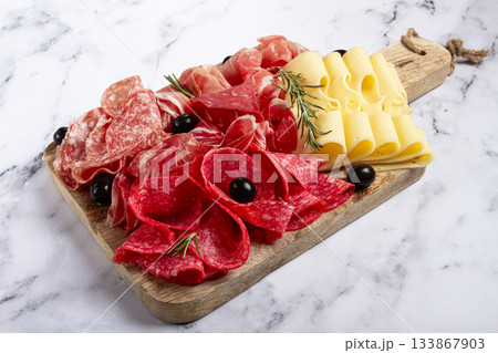 Assorted meat, appetizer, prosciutto, salami and ham, with maasdam cheese and olives, on a wooden board, breakfast, top view, close-up, no people 133867903