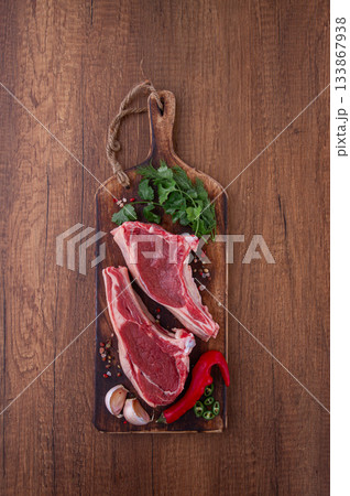 Freshly sliced lamb chops, with herbs and vegetables, on a wooden board, ready to cook, on a wooden table, Freshly sliced lamb chops, with herbs and vegetables, on a wooden board, ready to cook, on a wooden table, 133867938