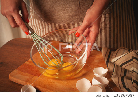 Whisking fresh eggs in a clear bowl on a wooden countertop during morning cooking session Whisking fresh eggs in a clear bowl on a wooden countertop during morning cooking session 133867987